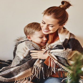 mother and son hug and laugh wrapped in a warm blanket