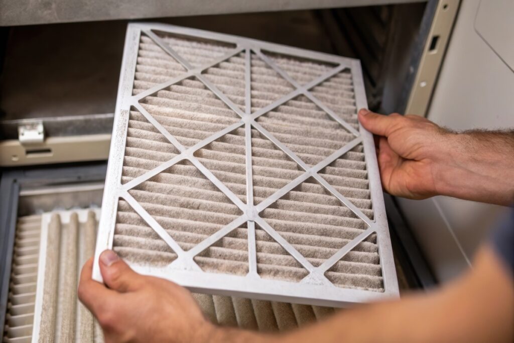 A closeup image showing a technicians hands cleaning a filter in an air handling unit with dust and debris visible on the filter material